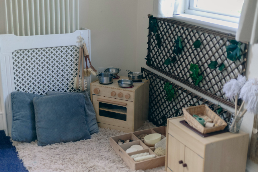 Miniature wooden kitchen set and sensory play items on a rug.