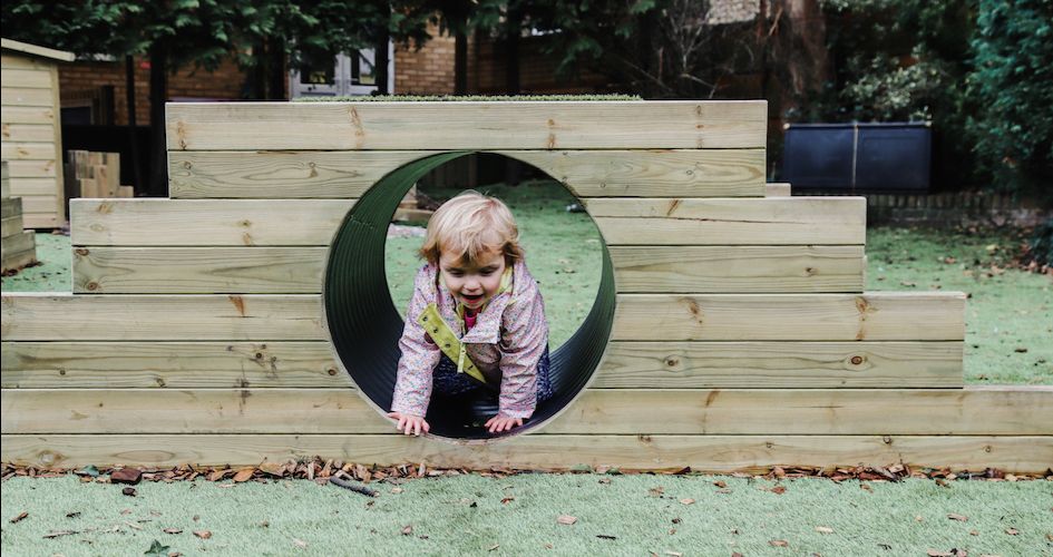 A toddler is seen crawling through a tunnel in an outdoor play area.