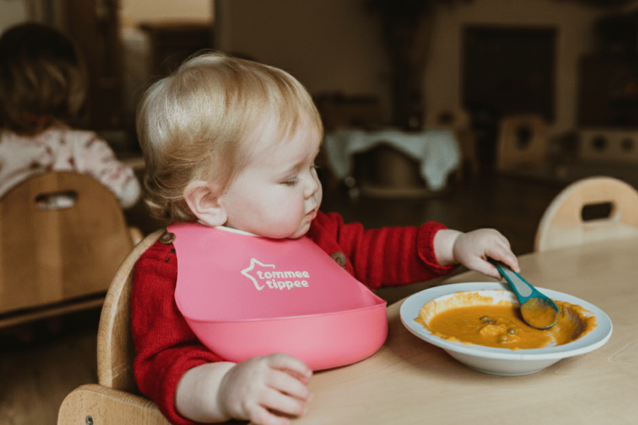 a toddler is feeding herself soup with a spoon