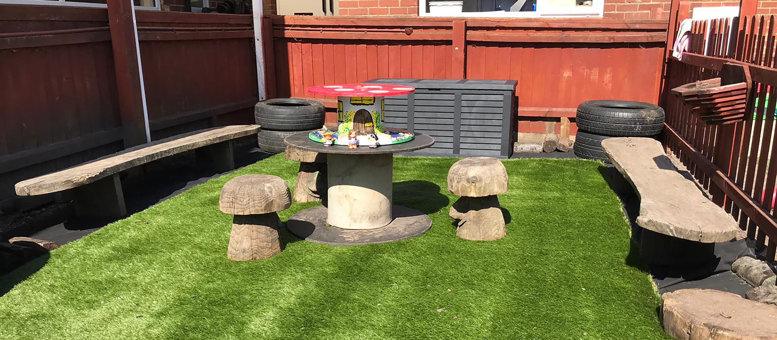 A bright and spacious nursery room with wooden floors, low tables and chairs, a teepee, and various play and learning stations.