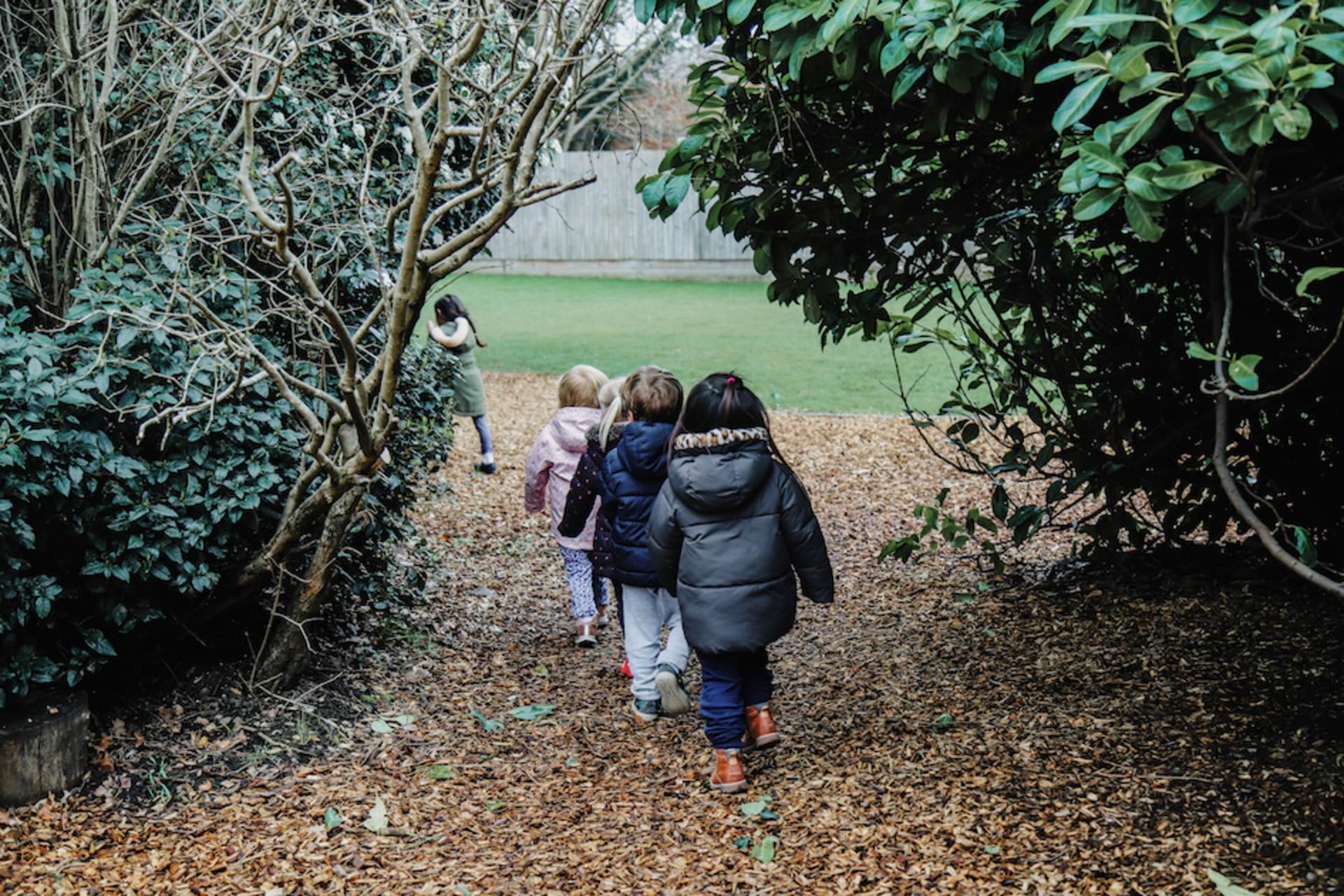 A group of children are walking single-file along a leafy path in a garden at the nursery.