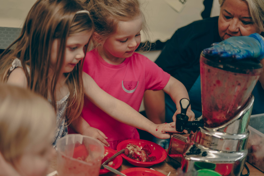 Children are heloing an adult to blend fruit for smoothies