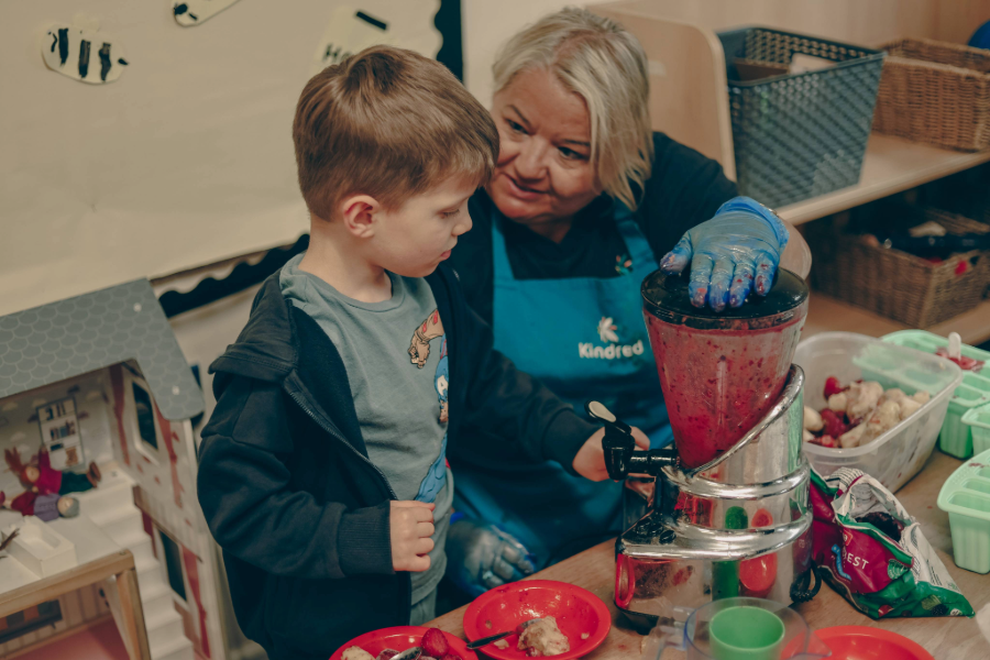 Adult and boy using a blender to make a fruit smoothie indoors.