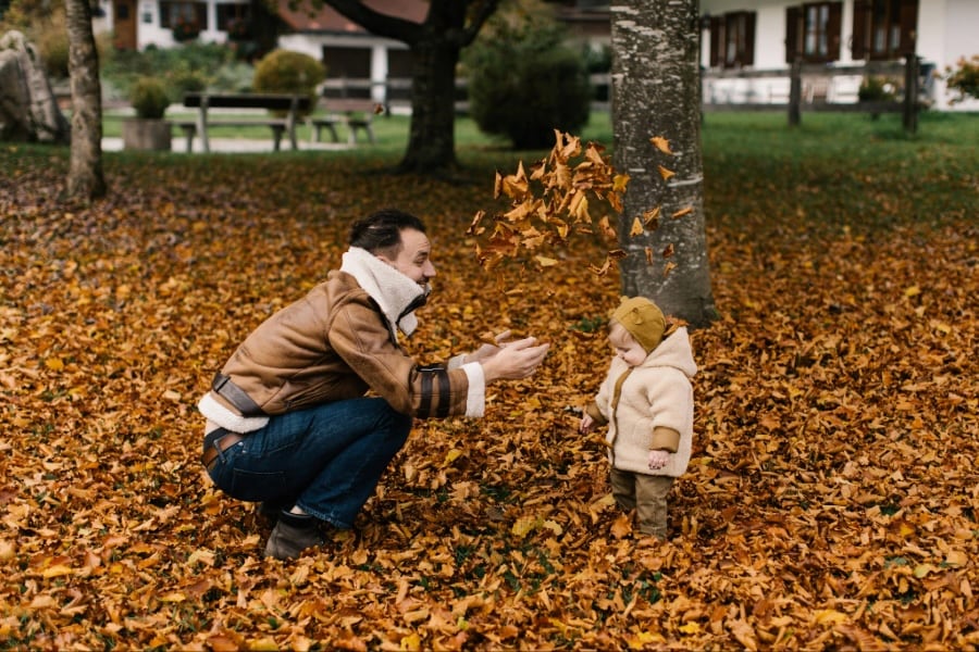 A man throws fallen leaves over a toddler in the park