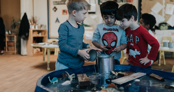 A group of children gathered and playing around a water table activity