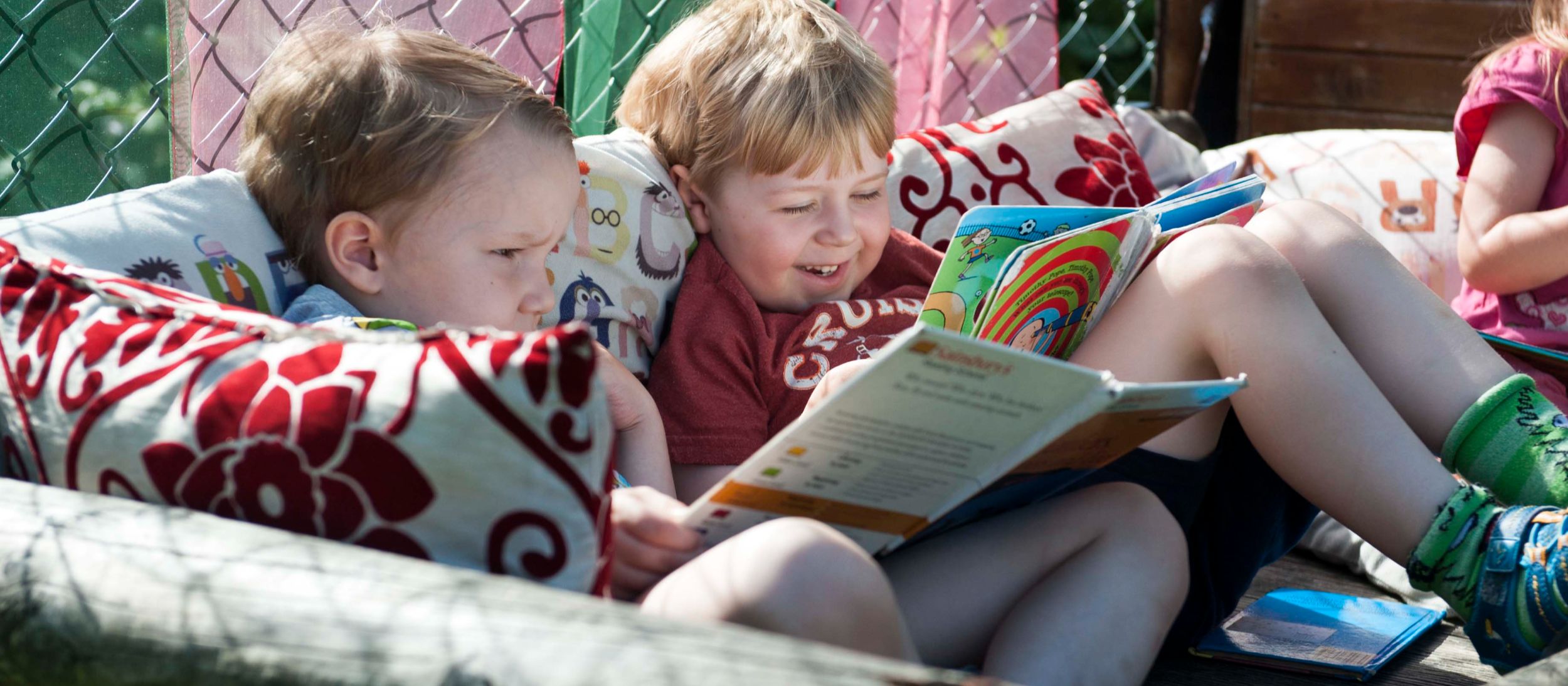 Two children reading and smiling on the sofa outside