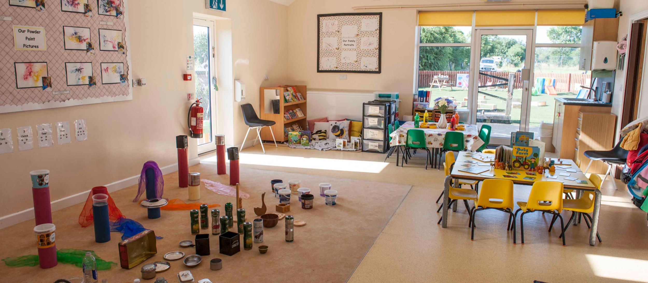 A bright, sunlit room at the nursery with low tables and chairs, an area for creative play, and displays of children's artwork on the wall.