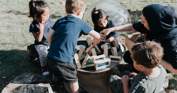 A group of children and a member of staff playing with natural wooden resources outside