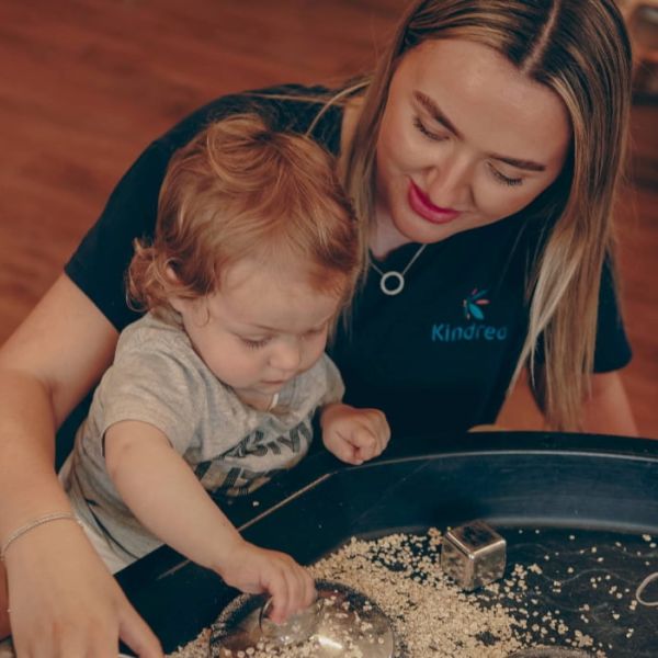 A baby an adult play with a sensory tuff tray 