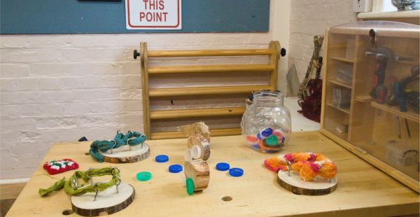 A close-up view of a workbench with loose parts like bottle caps, yarn, and natural materials for creative projects.