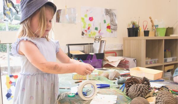 A child is working on a craft project at a table covered with art supplies and natural materials.