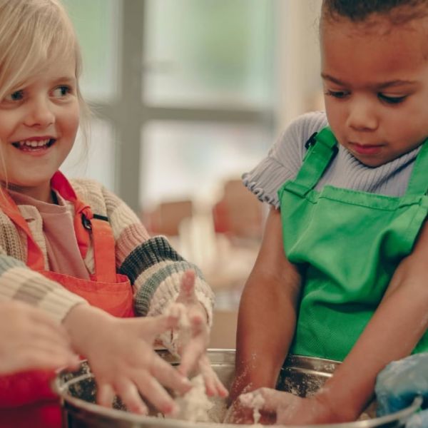 Two girls are mixing flour in a bowl with their hands