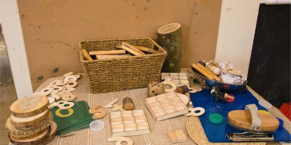 A table full of natural, loose-part materials for play, including a basket of sticks, wood slices with numbers, and other wooden toys.