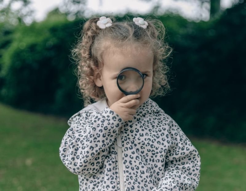 A little girl looks through a magnfying glass outside