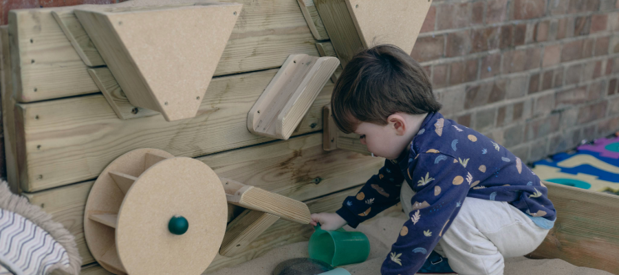 Boy playing in a sandbox with a wooden sensory wall.