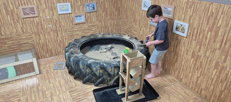 Boy playing in an indoor sand pit made from a large recycled tire.