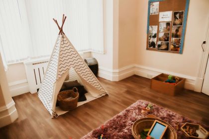 A cozy play corner at the nursery with a teepee tent, a furry rug, and a basket of toys.