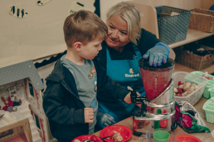 Adult and boy using a blender to make a fruit smoothie indoors.