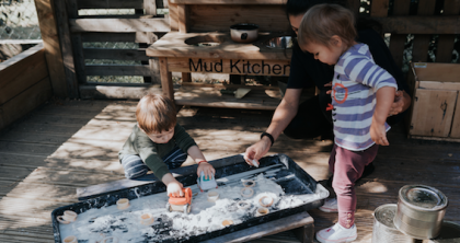 Children and a member of staff outside doing messy play in a tuff tray